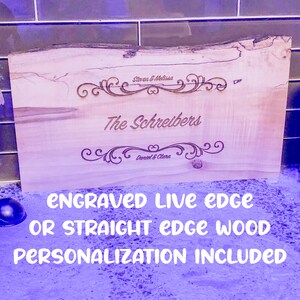 May include: A personalized wooden sign with a live edge. The sign is engraved with the text "The Schreibers" and two names with the words "Steven & Melissa" and "Daniel & Clara". The sign is made of light brown wood with a natural grain pattern. The text is in a dark brown color. The sign is perfect for a home or office.