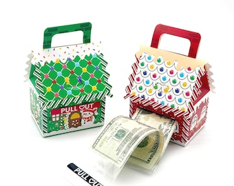 May include: Two house-shaped cardboard gift boxes with handles, one green and one red, featuring colorful roof patterns and snowman graphics. The red box has a clear plastic sleeve extending from the front, containing US dollar bills.
