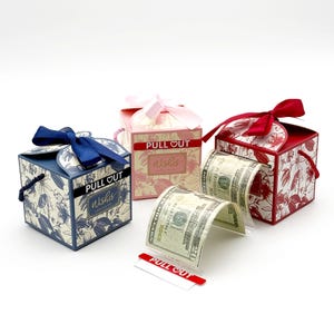 May include: Three small gift boxes with floral patterns and pull-out tabs that say "PULL OUT Wishes". The boxes are blue, pink, and red. A dollar bill is pulled out of the red box.