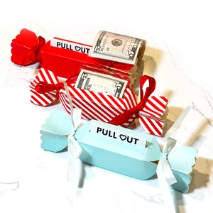 May include: Three red and white striped candy cane shaped boxes with a blue candy cane shaped box. Each box has a white ribbon and a black label that says "PULL OUT" with a heart symbol. The red and white boxes contain dollar bills.