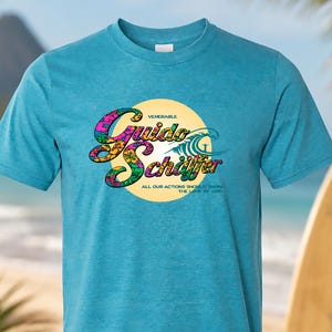 May include: A turquoise short-sleeve t-shirt featuring a yellow circular graphic with the text "Venerable Guido Schäffer" in a floral pattern, a wave illustration, and the text "ALL OUR ACTIONS SHOULD SHOW THE LOVE OF GOD" printed below.