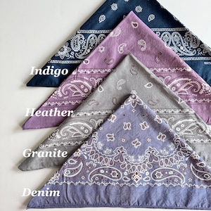May include: Four paisley bandanas in different colors: indigo, heather, granite, and denim. The bandanas are folded in a triangle shape and stacked on top of each other.