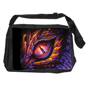 May include: Black messenger bag featuring a vibrant, artistic depiction of a dragon's eye. The eye is rendered in shades of purple, orange, and yellow, with a detailed, textured design. The bag has a black adjustable shoulder strap and a buckle closure.