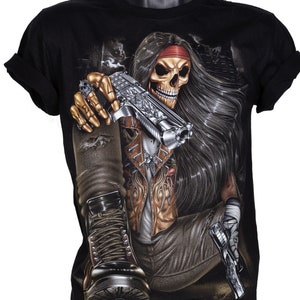 May include: Black t-shirt featuring a graphic print of a skull with long black hair wearing a red bandana, holding a gun and sitting with one leg crossed. The skull is wearing a brown leather jacket and jeans.