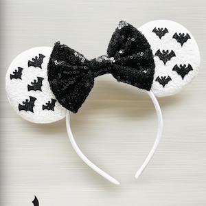 May include: White headband with black sequin bow and black bat ears. Each ear is white with black bat silhouettes.
