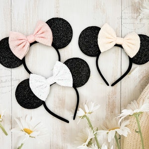 May include: Two pairs of black glitter Minnie Mouse ears with a headband. One pair has a pink lace bow and the other has a white lace bow.
