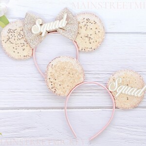 May include: Two pink headbands with gold glitter mouse ears and white "Squad" lettering.