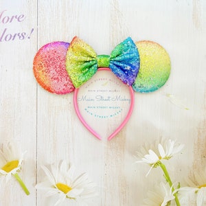 May include: Rainbow sequined Minnie Mouse ears headband with a pink headband and a large rainbow bow. The headband says "Main Street Mickey" on it.