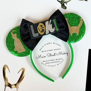 Pode incluir: Orelhas de rato verdes e pretas com detalhes em glitter dourado e um logotipo dourado do Loki. A faixa de cabeça é verde e diz "Main Street Mickey" em texto preto.