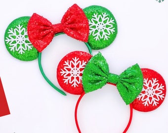 May include: Red and green Christmas-themed Minnie Mouse ears with a green sequin bow and white snowflake designs on the ears. The headband is red.