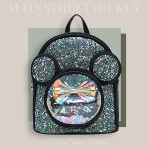 May include: A black glitter backpack with a clear plastic window on the front. The window shows a rainbow bow and colourful confetti. The backpack has black ears on the top and the text "Main Street Mickey" is printed on the bottom.