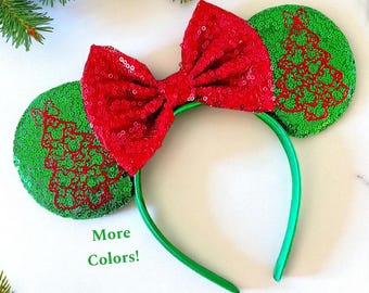 May include: A festive headband with green sequined ears featuring a red Christmas tree design. A large red sequined bow sits atop the green headband. The text "More Colors!" is displayed in green.