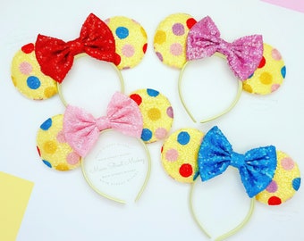 May include: Three pairs of yellow, red, and blue polka dot Minnie Mouse ears with matching bows. The bows are made of sequins and the ears are made of felt.