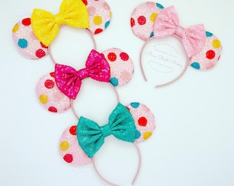 May include: Three pairs of pink Minnie Mouse ears with colorful polka dots and different colored bows. The bows are yellow, pink, and teal.