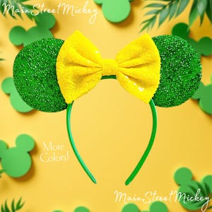 Può includere: Fascia per capelli con orecchie di Minnie Mouse in paillettes verdi e gialle con una fascia verde. La fascia ha un grande fiocco giallo con paillettes verdi.
