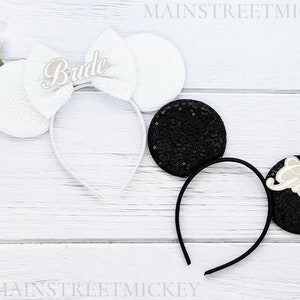 Puede incluir: Diadema blanca con orejas de novia con lazo blanco y la palabra "Bride" en cursiva. Diadema negra con orejas de novio con la palabra "Groom" en cursiva. Un conjunto de diademas de orejas blancas y negras.