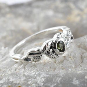 May include: A silver ring featuring a green gemstone set within a leafy design.