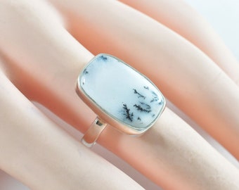 May include: A silver ring with a white and black dendritic agate stone. The stone is rectangular and has a smooth, polished surface.