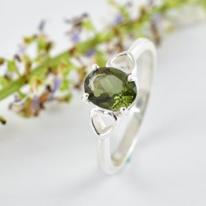 May include: A silver ring featuring a green oval gemstone set in a heart-shaped design.