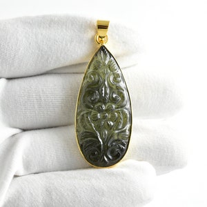 Op de afbeelding: Een traanvormige hanger met een gouden zetting en een gegraveerde groene edelsteen. De edelsteen heeft een bloemmotief.