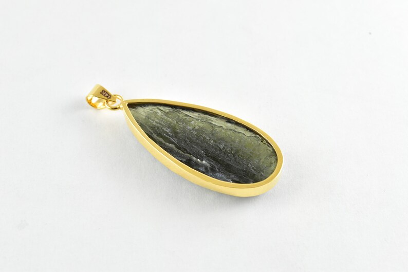 Op de afbeelding: Een gouden hanger met een traanvormige groene steen. De steen heeft een marmerpatroon en is gezet in een gouden bezel.