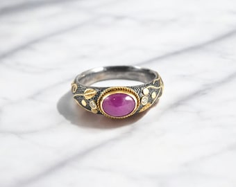May include: A silver ring with a pink gemstone set in a gold bezel. The ring is decorated with gold leaves and small white gemstones.