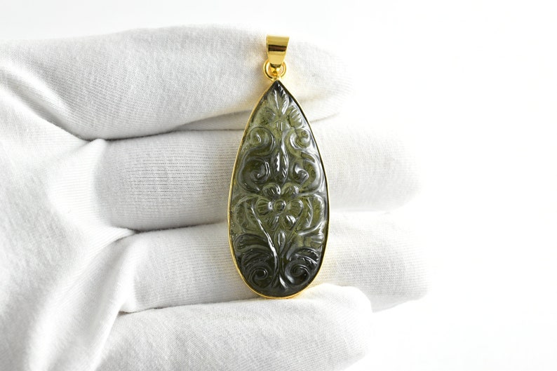 Op de afbeelding: Een traanvormige hanger met een gouden zetting en een gegraveerde groene edelsteen. De edelsteen heeft een bloemmotief.