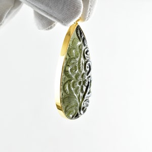 Op de afbeelding: Een traanvormige hanger met een gegraveerd bloemenmotief in een groene edelsteen. De hanger is gezet in een gouden frame.