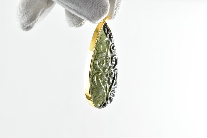 Op de afbeelding: Een traanvormige hanger met een gegraveerd bloemenmotief in een groene edelsteen. De hanger is gezet in een gouden frame.