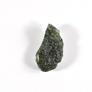May include: A dark green, rough, and irregularly shaped piece of moldavite, a type of tektite.
