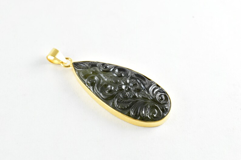 Op de afbeelding: Een donkergroene edelsteen hanger met een gouden zetting. De edelsteen is gegraveerd met een bloemmotief.