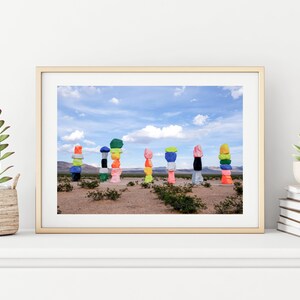 Puede incluir: Una fotografía enmarcada de formaciones rocosas coloridas apiladas en un paisaje desértico. Las rocas están pintadas en varios colores, incluyendo rosa, verde, azul, amarillo y naranja. El cielo es azul con nubes blancas.