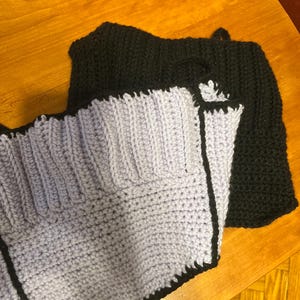May include: Two crocheted pieces of fabric, one lavender and one black, are sewn together. The lavender piece has a black border.