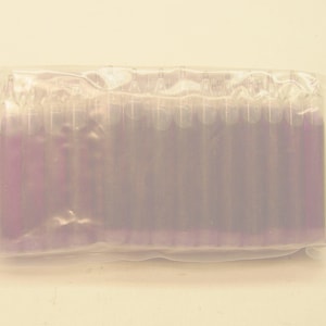 May include: A clear plastic package containing multiple purple-colored items. The items are arranged in a row, and the package is sealed. The items appear to be cylindrical in shape. The background is a light beige color.