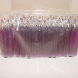 May include: A clear plastic bag containing a large quantity of small, cylindrical glass ampoules filled with a vibrant purple liquid. Each ampoule features a tapered, sealed top and a flat base, arranged in a dense, upright formation within the packaging.