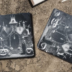 May include: Two black slate coasters with a Halloween theme. One coaster features a spooky house with a figure in front of it and pumpkins. The other coaster features a spooky house with pumpkins and bats.