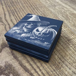 May include: Set of four black coasters with a white design of a skull wearing a witch's hat and pumpkins.
