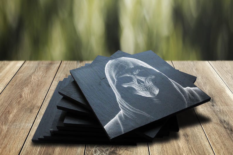May include: A set of black slate coasters with a white drawing of a hooded figure with a skull face. The coasters are stacked on a wooden surface.