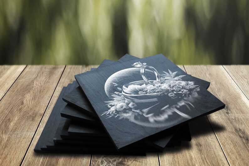 May include: A stack of black slate coasters with a white engraved design of a ring and flowers.