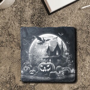 May include: Black and white Halloween-themed slate coaster featuring a spooky house with a full moon and bats flying overhead.  The house has a pointed roof and windows.  There are pumpkins in the foreground.