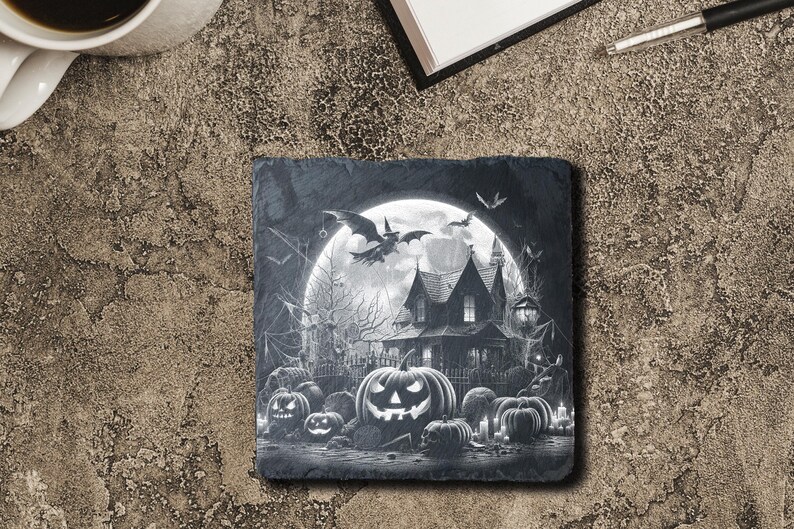 May include: Black and white Halloween-themed slate coaster featuring a spooky house with a full moon and bats flying overhead.  The house has a pointed roof and windows.  There are pumpkins in the foreground.