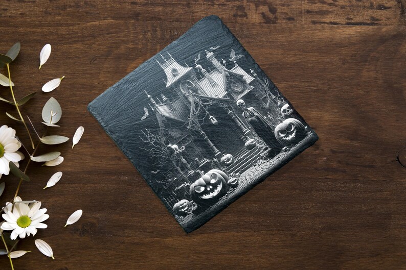 May include: A black and white image of a spooky house with a witch and pumpkins. The house is decorated with cobwebs and bats. The image is printed on a black slate coaster.