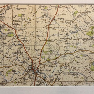 Könnte beinhalten: Eine Vintage-Karte der Cotswolds-Region in England mit der Stadt Malmesbury. Die Karte ist auf cremefarbenem Papier mit braunen, blauen und grünen Linien und Text gedruckt. Die Karte zeigt Straßen, Flüsse und Städte.