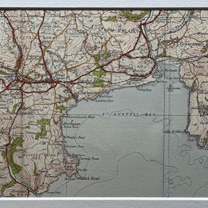 Peut inclure: Une carte vintage de la baie de St. Austell en Cornouailles, en Angleterre. La carte montre le littoral, les villes et la campagne environnante. La carte est imprimée en encre noire, brune et verte sur un fond blanc.