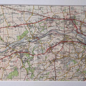 May include: A framed vintage map print showing a detailed topographical map with roads, rivers, and place names. The map is in beige, green, and brown, with red lines marking major routes. The print is in a white frame.
