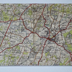 Könnte beinhalten: Eine Vintage-Karte von Horsham, England, mit roten Linien, die Straßen anzeigen, und einem beigefarbenen Hintergrund. Die Karte zeigt die Stadt Horsham und die umliegenden Gebiete, darunter die Städte Warnham, Broadbridge Heath und Slinfold.