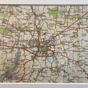 Peut inclure: Une carte vintage de Chichester, en Angleterre, avec des routes rouges et du texte jaune. La carte montre les villes et villages environnants, y compris Bosham, Tangmere et West Hampnett. La carte est intitulée "Chichester, Noviomagus."