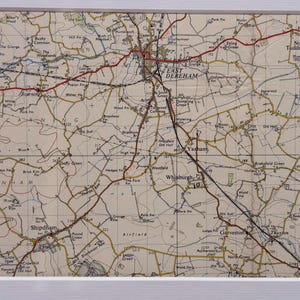 Może przedstawiać: Oprawiona mapa w stylu vintage z East Dereham, Norfolk, Anglia, z drogami, miastami i szczegółami geograficznymi. Mapa ma kremowe tło z brązowymi i czerwonymi liniami i jest zamknięta w białej ramie.