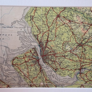 Puede incluir: Mapa vintage enmarcado de Liverpool, Inglaterra, con una representación detallada de la ciudad y sus alrededores. El mapa tiene una combinación de colores crema y verde con marcas de carreteras rojas, y está enmarcado en blanco.