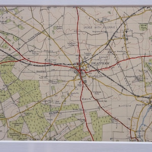 May include: A framed vintage map of the Swaffham area, showing roads, towns, and geographical features. The map has a beige background with black and red lines, and the town name "Swaffham" is visible. The map is framed in white.